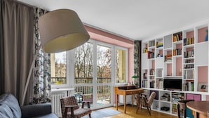 Ein Wohnzimmer mit einer Couch, einem Holztisch, einem Bücherregal und einem großen Fenster mit Blick auf Bäume.