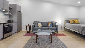 A compact living space with a kitchenette, a sofa, a glass coffee table, and a bed. - Spacious Studio Suite, Downtown Durham (Durham)