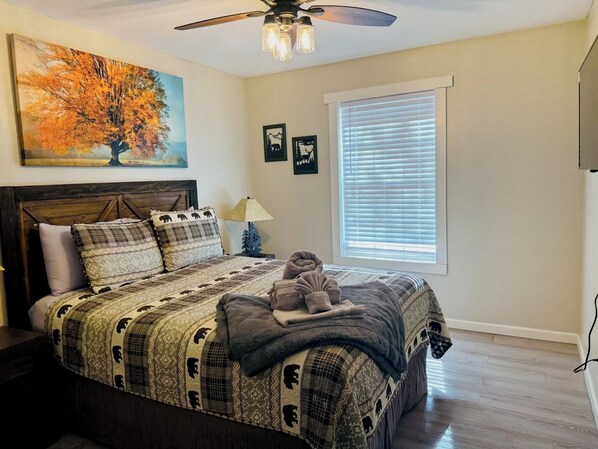 A bedroom with a bed, a ceiling fan, a window with blinds, and a painting on the wall. - Charming 3-bedroom Ruidoso cabin in a prime location with AC & WiFi. (Ruidoso)
