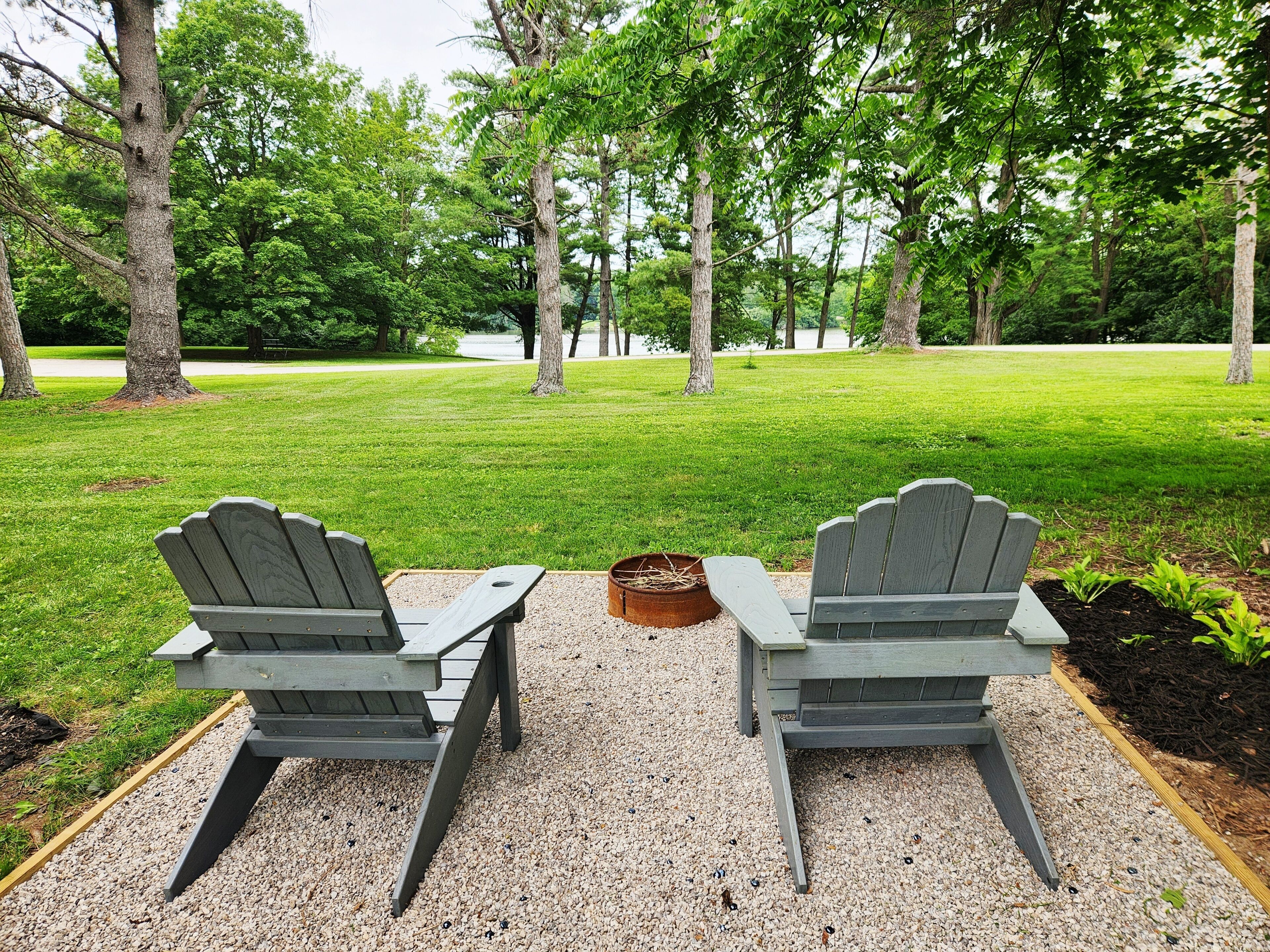 Two Adirondack chairs facing a grassy area with trees in the background.