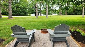 Two Adirondack chairs facing a grassy area with trees in the background.