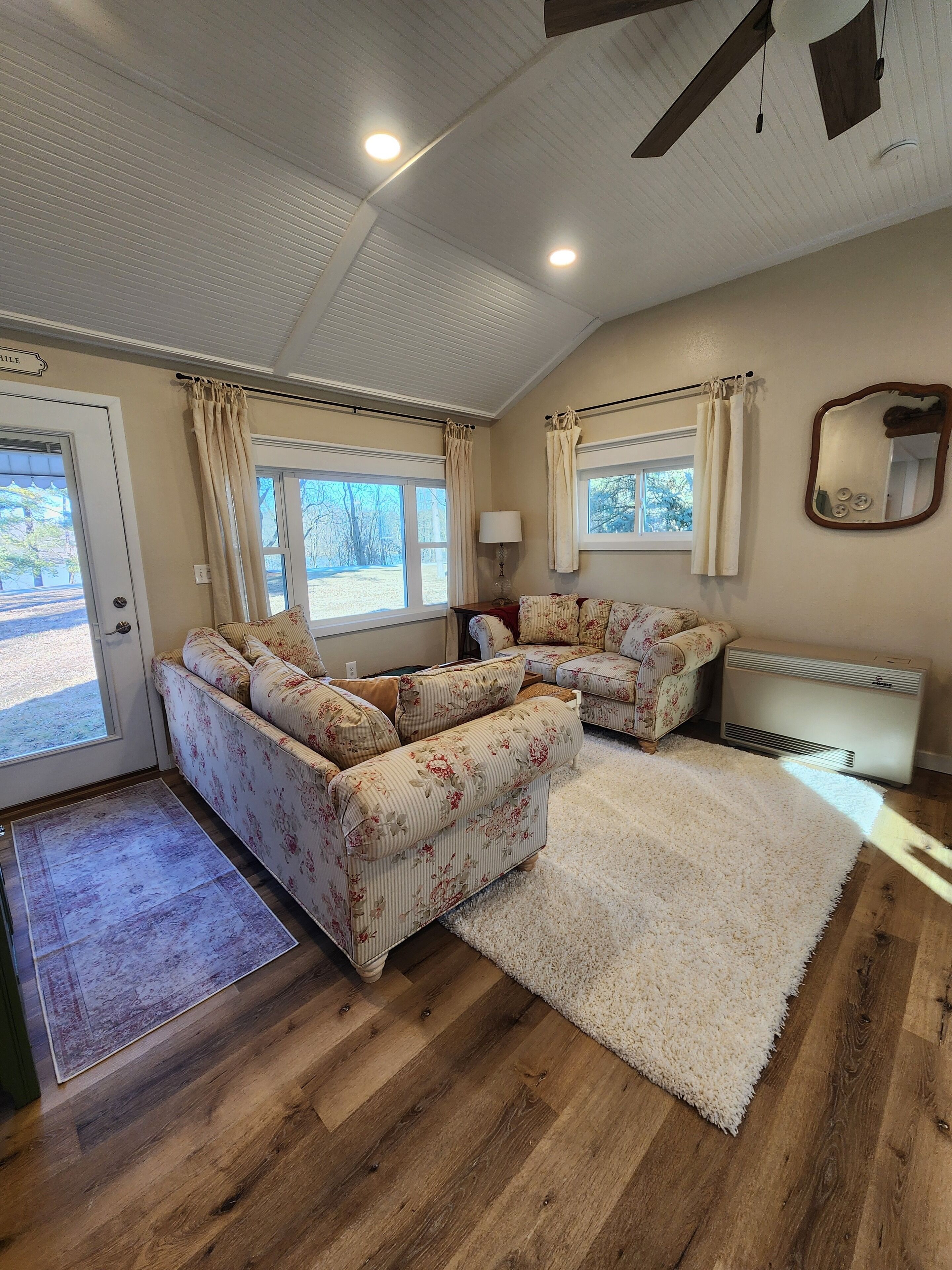 A cozy living room with a sectional sofa, a white rug, wooden flooring, and a ceiling fan.