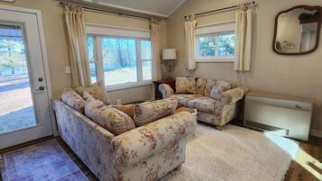 A cozy living room with a sectional sofa, a white rug, wooden flooring, and a ceiling fan.