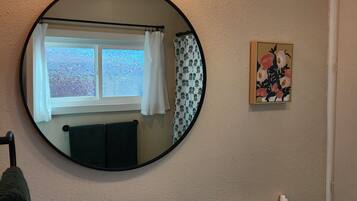 Une salle de bain avec un miroir rond, un lavabo, des toilettes et une fenêtre en verre dépoli.