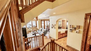 A spacious living area with a wooden staircase, a kitchen with a sink, and a dining area with chairs. - Luxury Ski-In/Ski-Out Empire Pass Retreat | Private Hot Tub | Sleeps 12 (Park City)