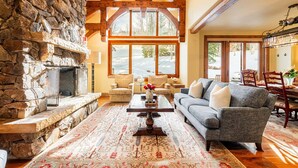 A stone fireplace, a large window, a sofa, and a patterned rug in a cozy living room. - Luxury Ski-In/Ski-Out Empire Pass Retreat | Private Hot Tub | Sleeps 12 (Park City)