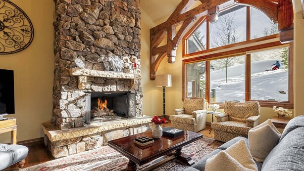 A cozy living room with a stone fireplace, large windows, and comfortable seating. - Luxury Ski-In/Ski-Out Empire Pass Retreat | Private Hot Tub | Sleeps 12 (Park City)