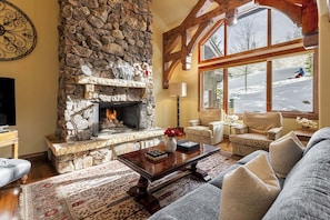 A cozy living room with a stone fireplace, large windows, and comfortable seating.
