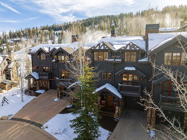 A large, multi-story log cabin with a stone foundation, multiple balconies, and a snow-covered roof.