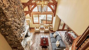 A high-ceilinged room with a stone wall, a chandelier, a patterned rug, a sofa, and a dining area with a table and chairs. - Luxury Ski-In/Ski-Out Empire Pass Retreat | Private Hot Tub | Sleeps 12 (Park City)