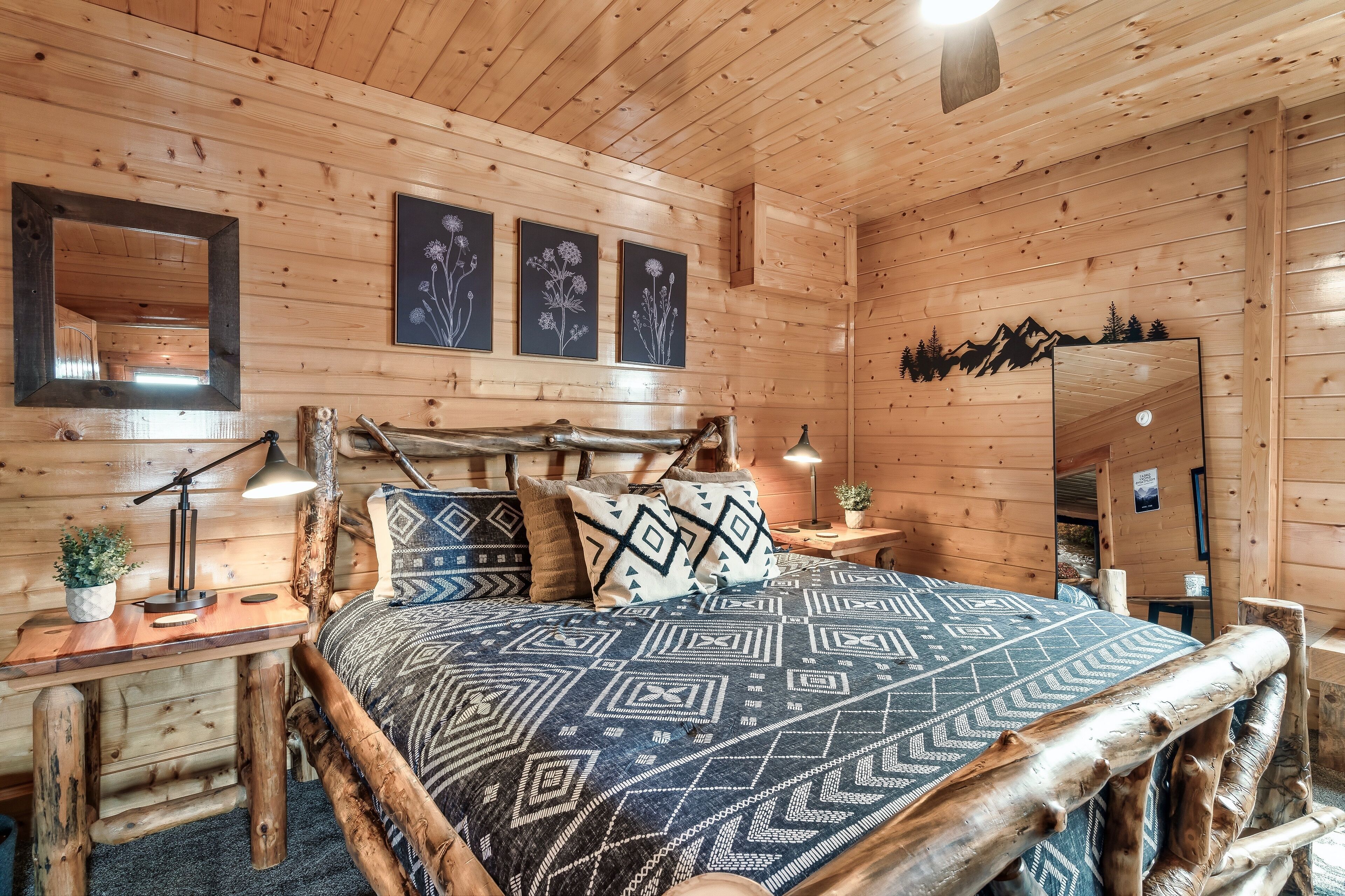 A wooden cabin bedroom with a bed, bedside tables, a mirror, and wall art.