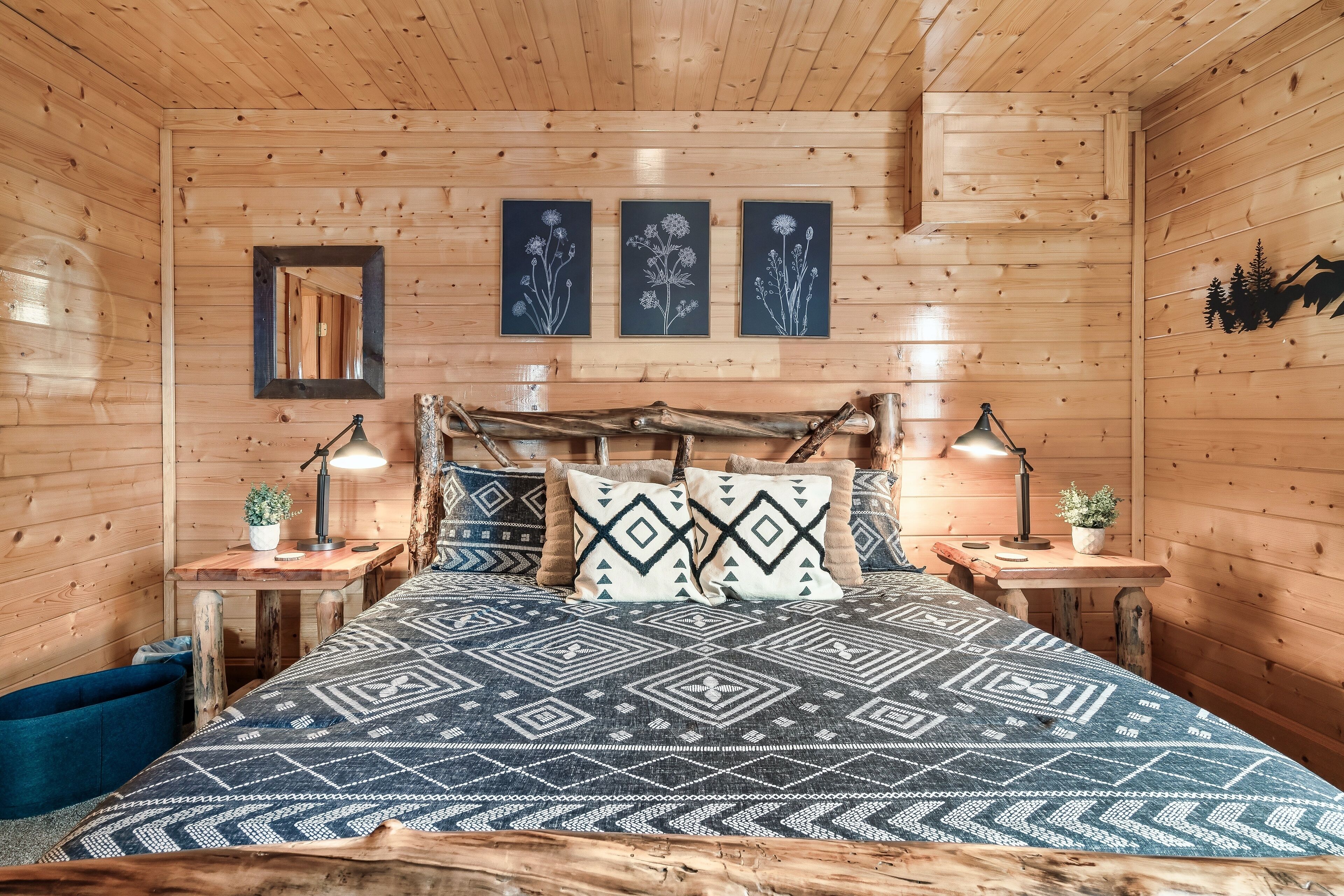 Een slaapkamer in een houten hutje met een bed, twee nachtkastjes, een spiegel en kunst aan de muur.