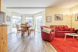 A living room with a red sofa, a wooden dining table with chairs, and large windows. - Störtebekerstraße 14 - Apartment 6 - Comfortable vacation apartment with terrace and (Zingst (Ostseeheilbad))