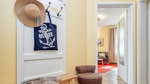 Un pasillo con un banco de madera, un sillón marrón y un perchero con sombrero y bolsa de tela.