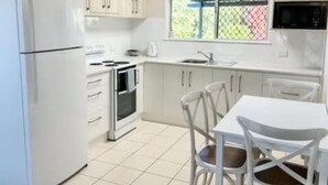A kitchen with white cabinets, a white refrigerator, a stove, a microwave, and a dining table with chairs. - Beachside on Burkitt - duex (Bargara)