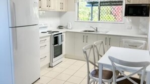 Een keuken met witte kastjes, een koelkast, een fornuis, een magnetron en een eettafel met stoelen.