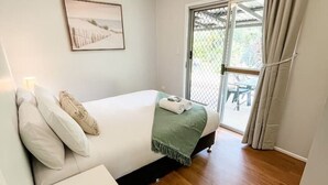 Een slaapkamer met een bed, een nachtkastje, een plafondventilator, een raam met gordijnen, en een deur die uitkomt op een buitenruimte.