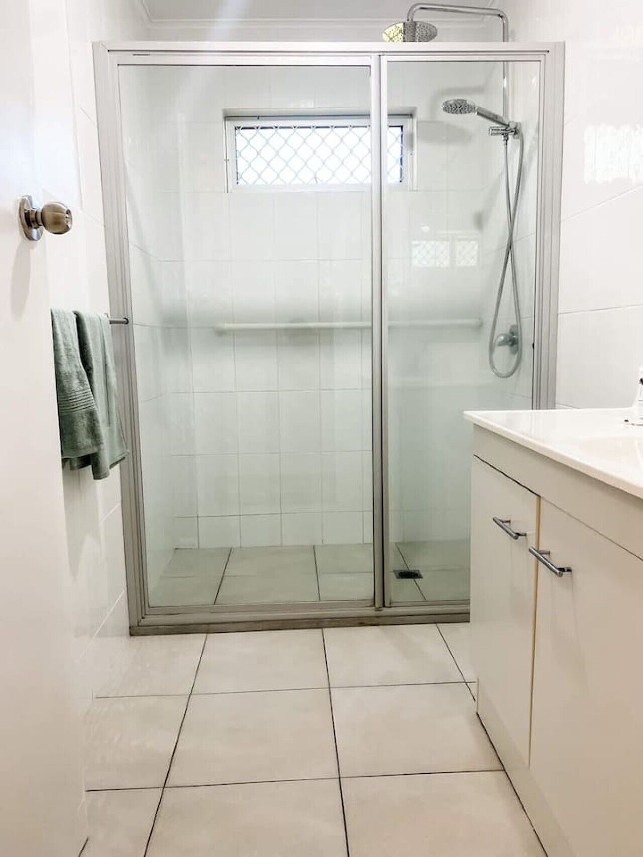 Une salle de bain moderne avec une douche à parois de verre, un sol carrelé de blanc et un lavabo doté d’un plan de travail.