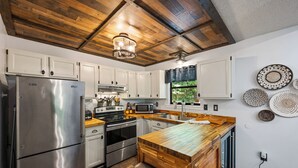 A modern kitchen with white cabinets, stainless steel appliances, a wooden island, and woven baskets on the wall.