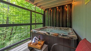 A hot tub with a wooden deck and a window view of a forest.