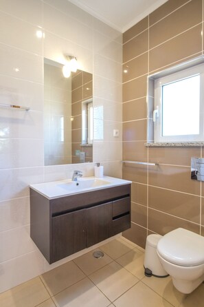 A modern bathroom with a large mirror, a sink, a toilet, and a window.