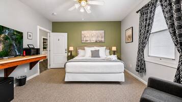 A bedroom with a bed, a desk, a television, a ceiling fan, and artwork on the walls.