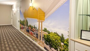 Un couloir d’hôtel avec un sol à carreaux, une vue sur le paysage urbain par une fenêtre et un certificat encadré accroché au mur.