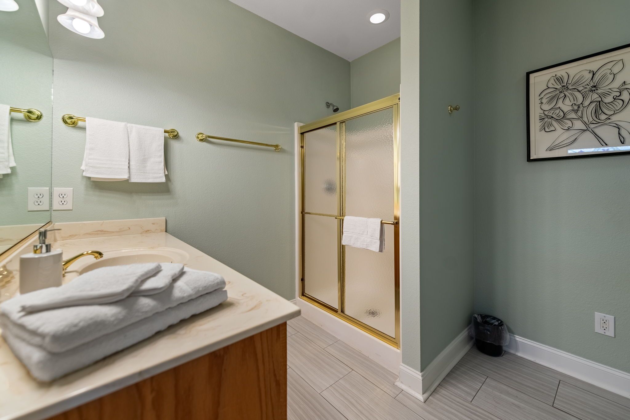A bathroom with a vanity, a glass shower enclosure, and a framed floral artwork on the wall.