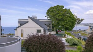 A residential area with a large tree, a white building with a grey roof, and a view of the sea. - 3 BR Holiday home - Steps to the lake and short, scenic stroll to town (Taupō)