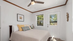Ein Schlafzimmer mit Bett, Deckenventilator, zwei Fenstern und einer Tür.