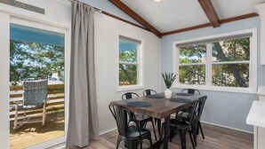 Ein Essbereich mit Holztisch und schwarzen Stühlen, großen Fenstern mit Vorhängen sowie Blick auf das Meer und Bäume.