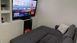 A modern living room with a flat-screen TV mounted on a white wall, a grey sofa, and a small black TV stand. - Beautiful, comfortable and relaxing house 15 min from Vineyards (El Sauzal)