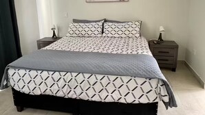 A neatly made bed with a geometric patterned bedspread and pillows, two bedside tables with lamps, and a painting of a beach scene on the wall. - Beautiful, comfortable and relaxing house 15 min from Vineyards (El Sauzal)