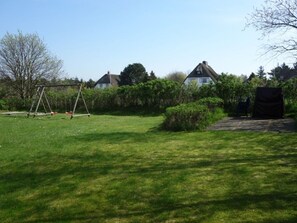 Ein gräserner Garten mit Schaukel, Geräteschuppen und einem Haus im Hintergrund.