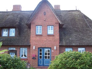 A red brick building with a blue door and windows, surrounded by greenery. - Bredland Vacation Apartment - Bredland Vacation Apartment in Nieblum - Enjoy the Sea Air (Nieblum)