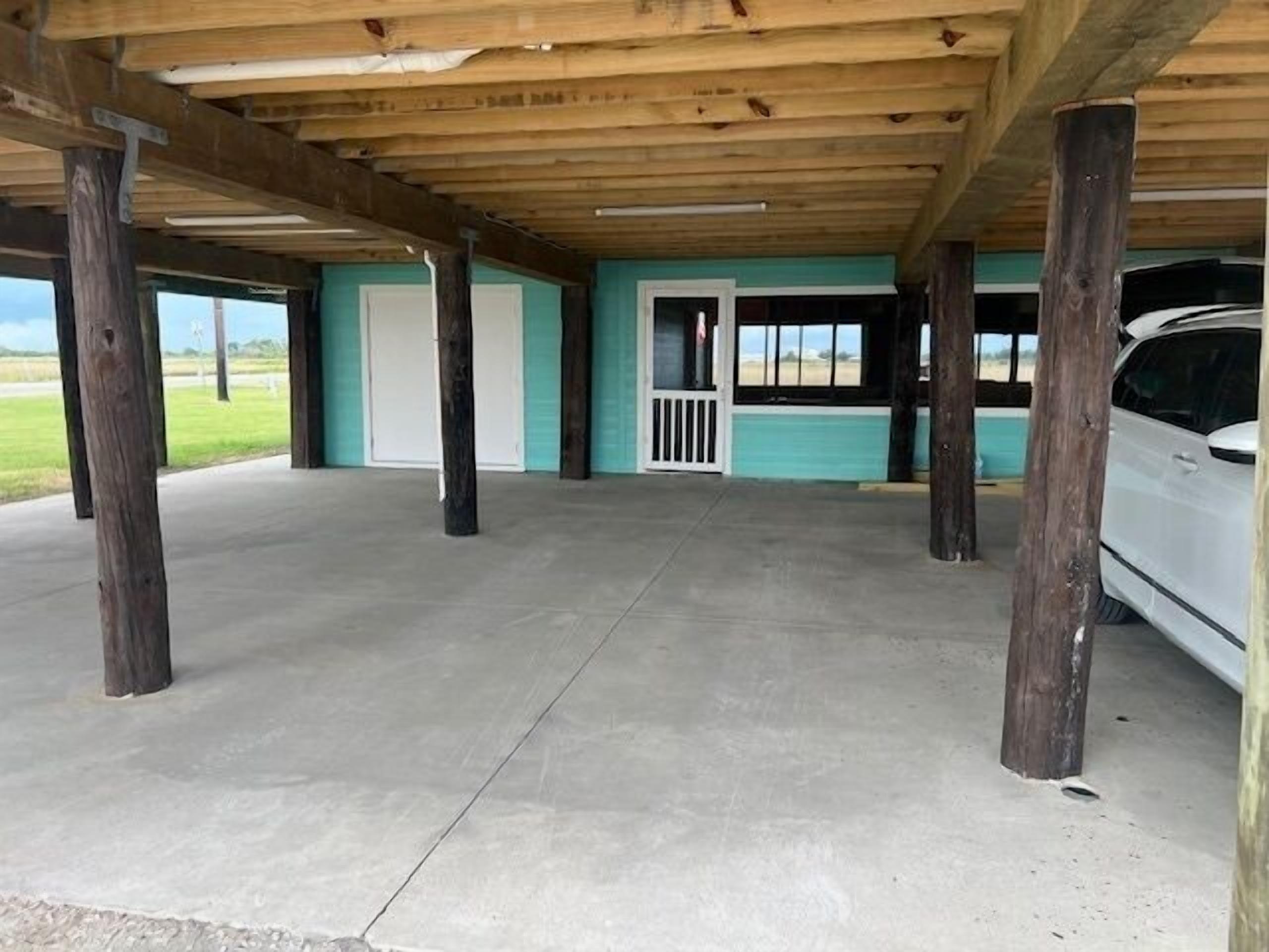 An open garage with a concrete floor, wooden beams, and a white car parked inside.
