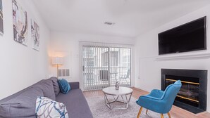 Una sala de estar moderna con un sofá gris, un sillón azul, una mesita de centro redonda y una chimenea.