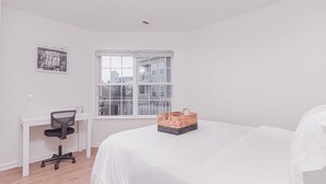 Un dormitorio con una cama, un escritorio con una silla, una ventana y un cartel motivacional enmarcado.