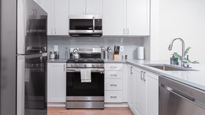Cocina moderna con armarios blancos, electrodomésticos de acero inoxidable y encimera negra.
