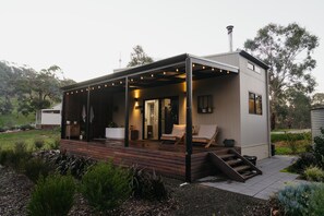 Una cabaña moderna con terraza de madera, mobiliario exterior y un porche cubierto.