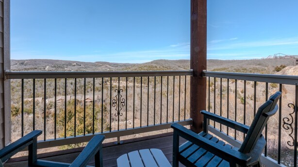A balcony with two Adirondack chairs and a view of a desert landscape.