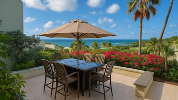 An outdoor patio with a table and chairs, a large umbrella, and a view of the ocean.