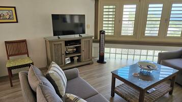 A living room with a sofa, a coffee table, a TV, and a window with blinds.