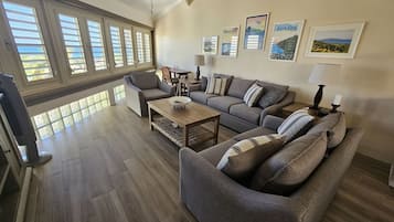 Een ruime woonkamer met een grijze zithoek, een houten salontafel, en een eethoek met een tafel en stoelen.