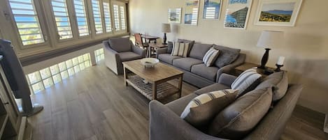 A spacious living room with a grey sofa set, a wooden coffee table, and a dining area with a table and chairs.