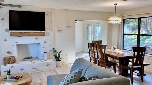 A modern living room with a fireplace, a dining area with a wooden table and chairs, and a large window offering a view of the outdoors. - Hilltop Harbor House (Granbury)