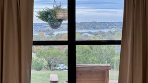 A window with a view of a lake, trees, and a wooden structure. - Hilltop Harbor House (Granbury)