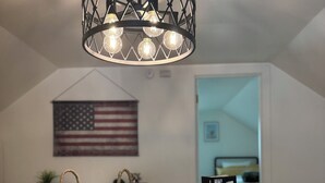 A room with a ceiling light fixture, a table with a jigsaw puzzle, a woven bag, and an American flag.