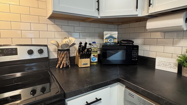A kitchen with white cabinets, a black stove, a microwave, and a dish rack.