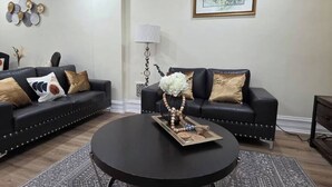 Un soggiorno con due divani in pelle nera, un tavolino rotondo con oggetti decorativi, un quadro astratto incorniciato e una lampada da terra.